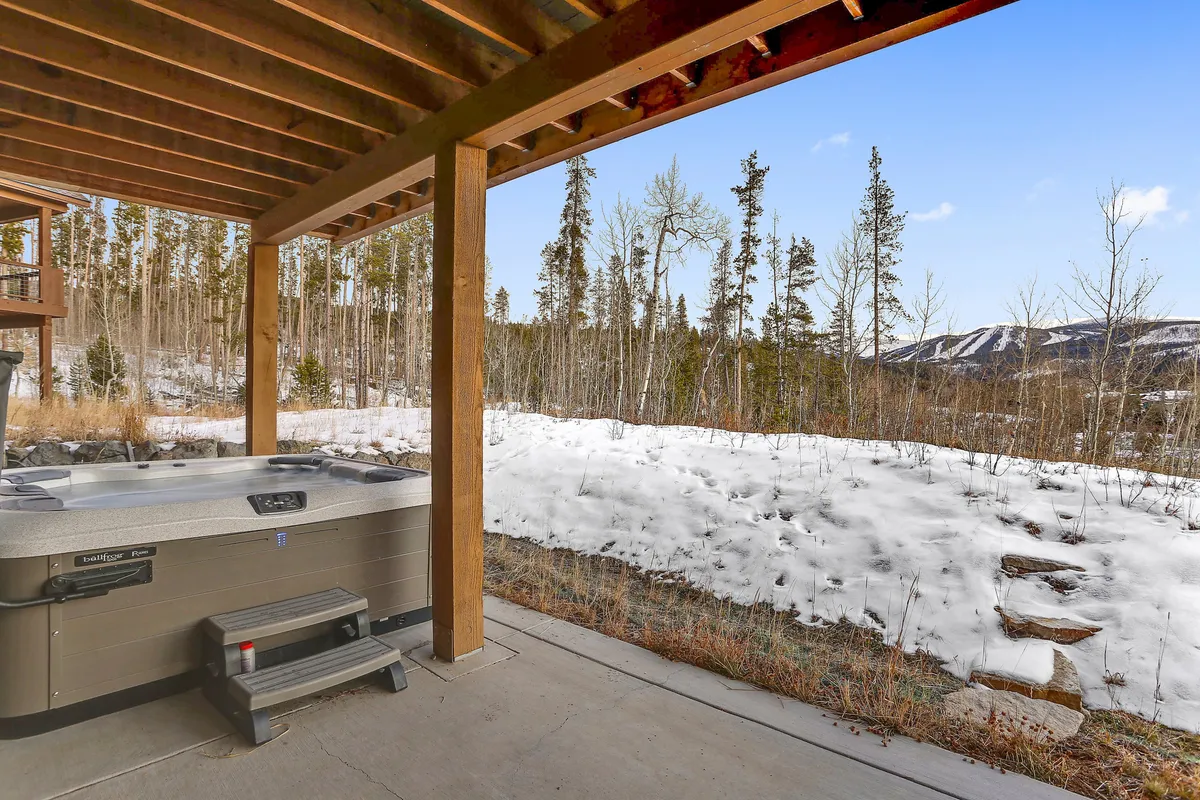 An inviting exterior shot of a private hot tub on a wooden deck, surrounded by snow-covered ground and distant trees, with wooden beams framing the view. The mood is tranquil, suggesting relaxation after a day of adventure, and hints at opportunities for stargazing or enjoying sunset mountain views.