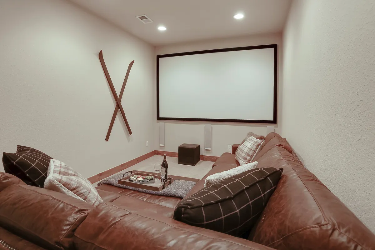 This image captures a luxurious home theater featuring a large projection screen, a plush leather sectional couch, cozy blankets, ski-themed decor, and a coffee table with snacks. The lighting is dim and inviting, perfect for movie nights or game nights.