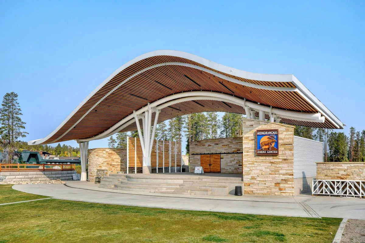 A dynamic outdoor venue with a curved roof structure and stone walls, set up for concerts or community gatherings. The stage area suggests a place for live performances, festivals, and large group events.