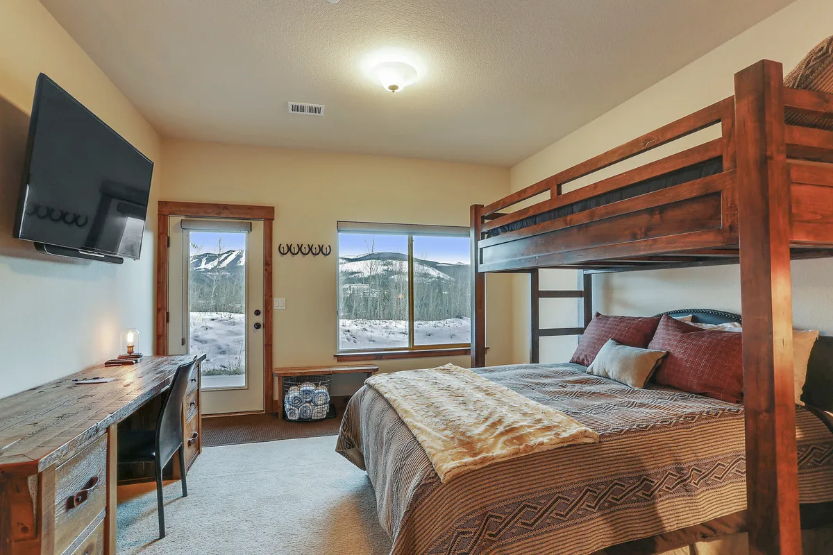 A tranquil bedroom with a bunk bed, a large window offering breathtaking mountain views, a sleek desk with a chair, and a flat-screen TV. The space is both family-friendly and functional, perfect for flexible sleeping arrangements and quiet retreats.