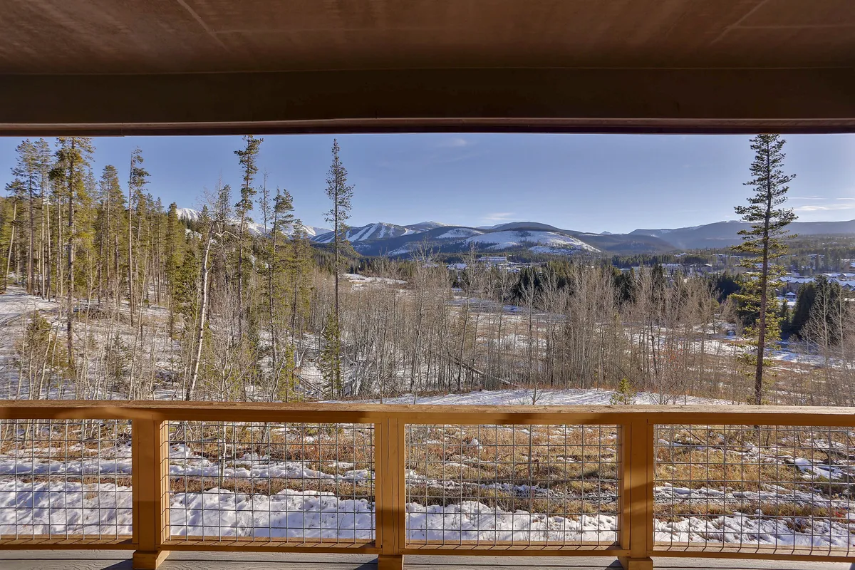 A panoramic view of a snow-capped mountain range, pine trees, and expansive snow-covered fields, seen from a wooden railing. This tranquil landscape invites activities like hiking, wildlife spotting, and photography, embodying the natural beauty of the Rocky Mountain area.