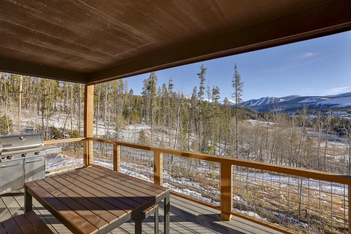 An exterior deck scene featuring a wooden table with seating and a grill, set against a scenic mountain and forest backdrop. The inviting setting is ideal for family barbecues, outdoor dining, or simply soaking up nature together. The image captures the appeal of spending quality time outdoors in the Rocky Mountains.