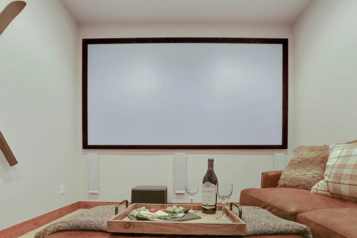 An intimate, luxurious home theater setup with a large blank screen, comfortable seating, a bottle of wine, and a tray of snacks. The space is designed for relaxation and private entertainment.