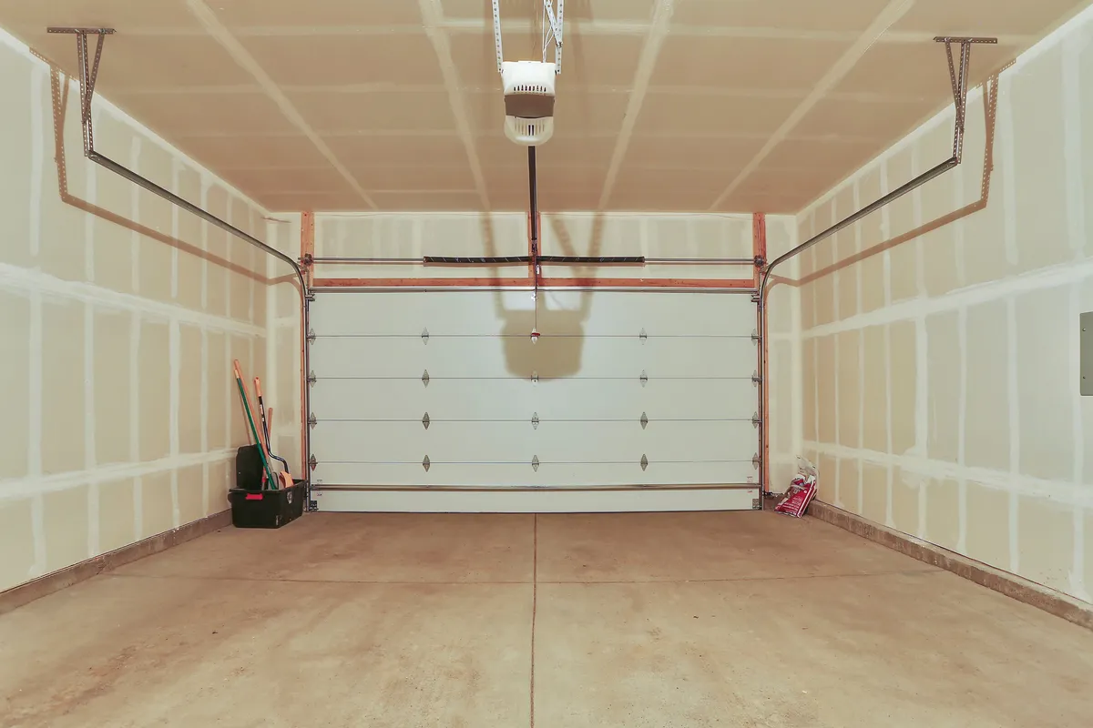 A functional garage featuring a garage door, an assortment of tools, and a storage box, highlighting the practical space available for storing sports gear such as bikes and skis, as well as parking vehicles.
